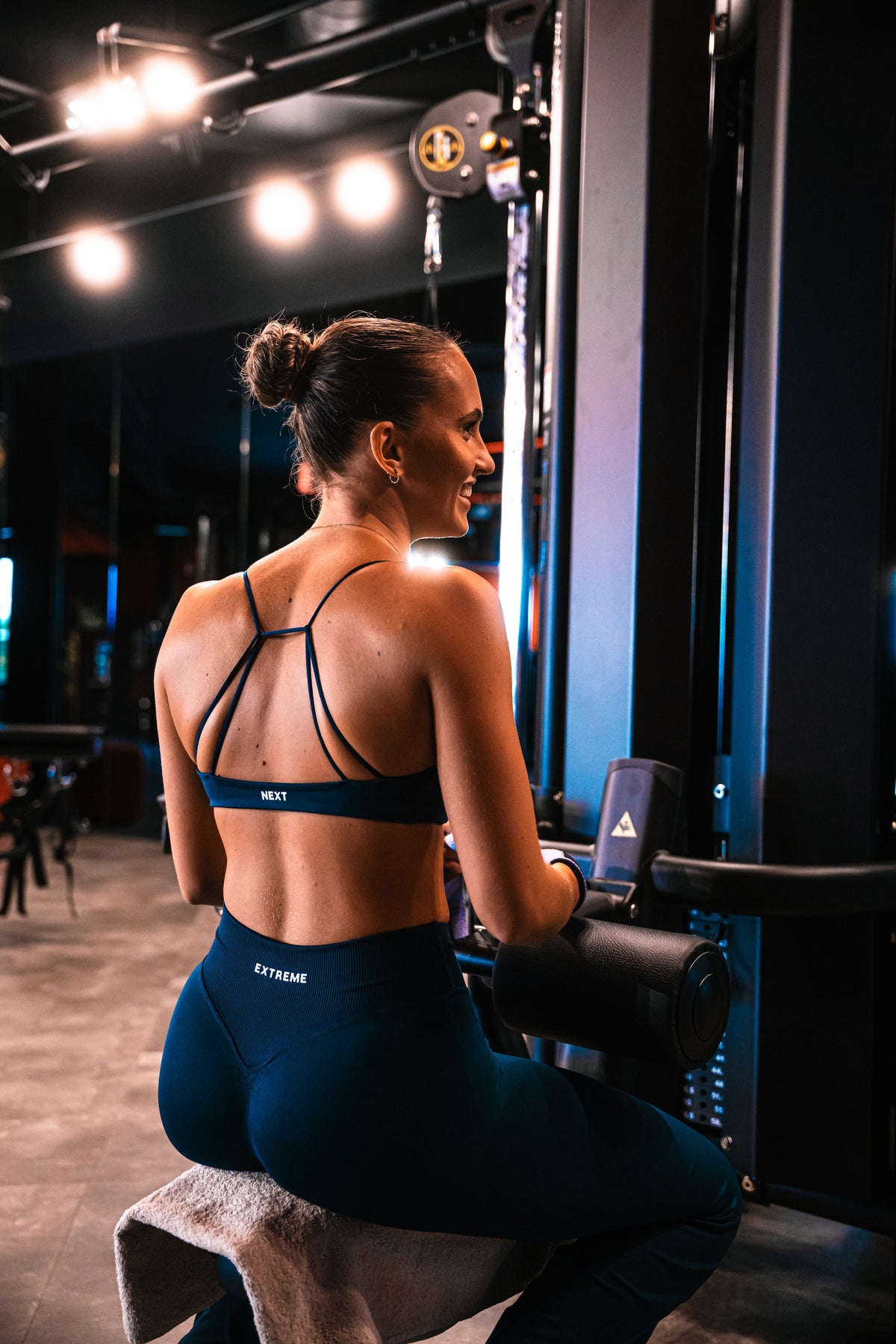 Atlete in de NEXT sport-bh en Cross Waist Legging in Abyss Blue op een machine in de gym