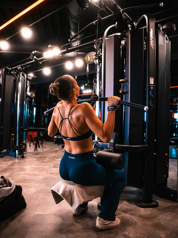 Atlete in de Flair Legging en Twist Front Bra in Abyss Blue bij een lat pulldown in de gym